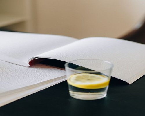 A glass of fresh water with lemon next to a book on a side table